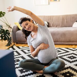 Pregnant woman doing seated stretch at home, showing the importance of physical therapy for pregnancy.