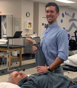 Photo of Luke Abney, PT, DPT, standing in front of a treatment table with a patient.