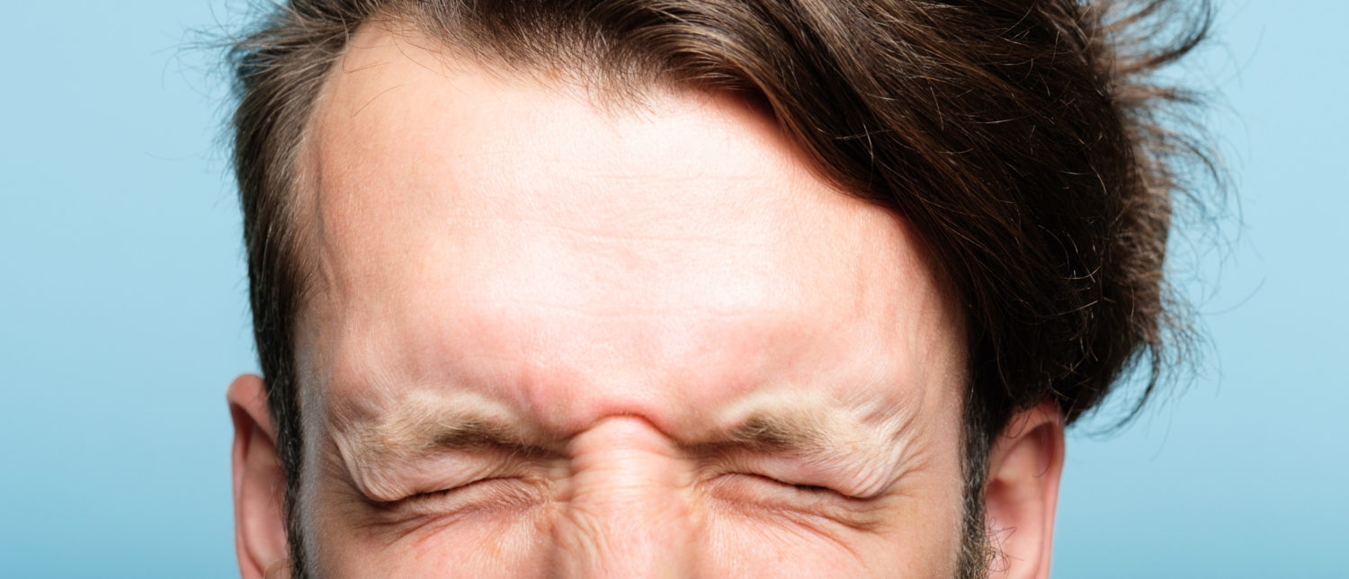 Man with a headache, holding his forehead and wincing in pain.