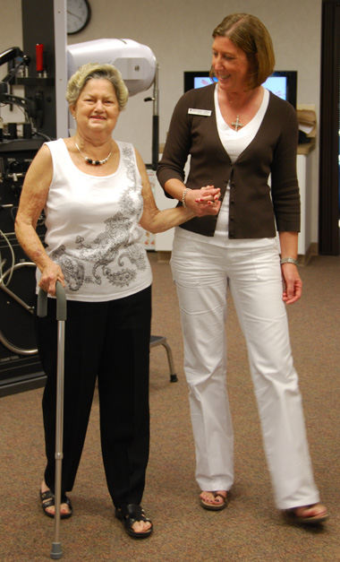 Image of a woman holding a female PT's hand during Epley maneuver physical therapy technique for vertigo treatment. The background shows medical equipment. This image represents a patient receiving vertigo treatment through physical therapy, including vertigo exercises and vertigo medicine.